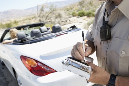 police officer writing a traffic ticket for a woman sitting in a white convertible car